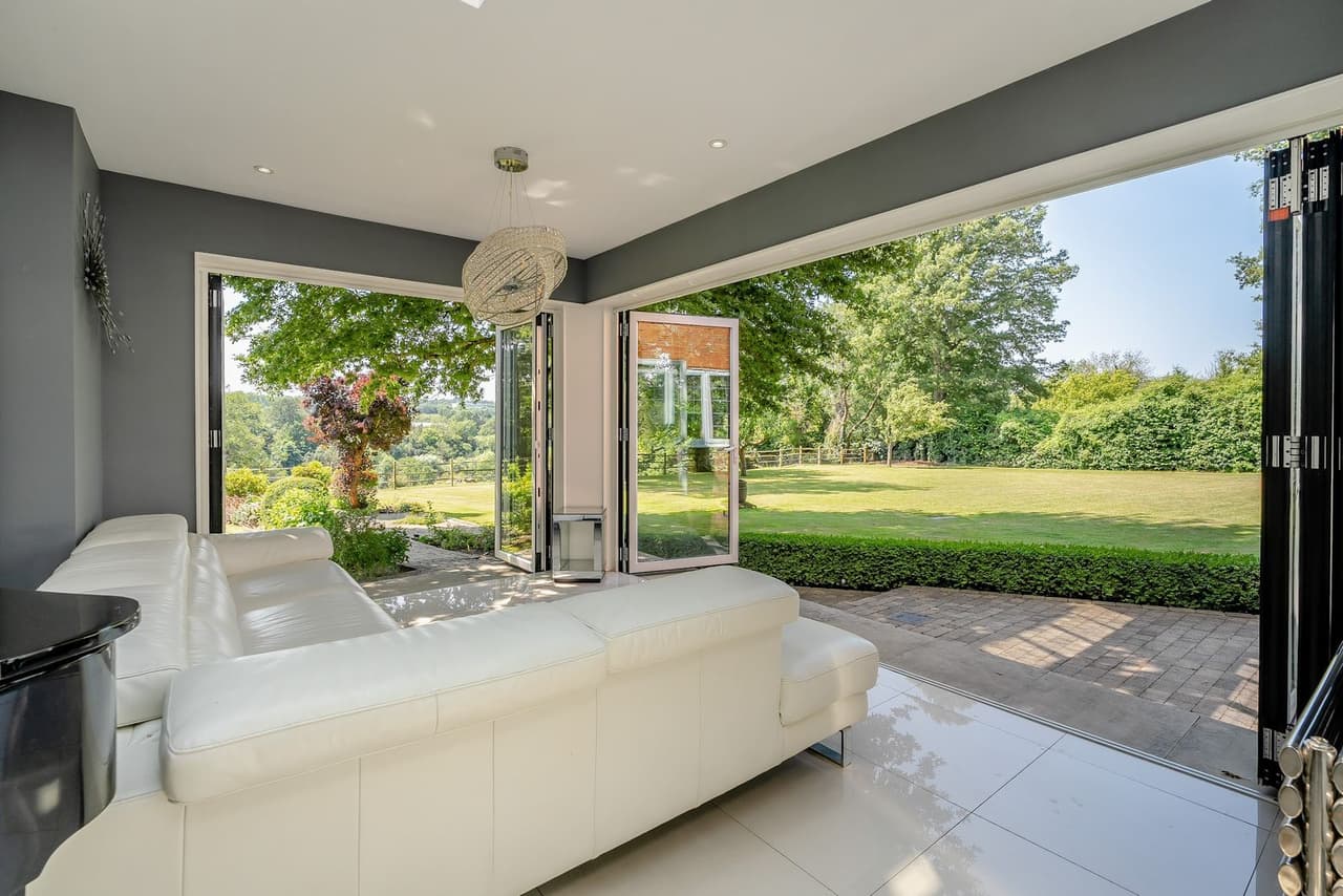 A living room with a white corner sofa and doors open to the garden
